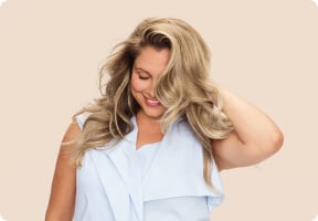 Femme touchant ses cheveux blonds volumineux avec balayage