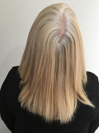 Avant la photo : vue arrière d’une femme aux cheveux blonds de longueur moyenne avec des mèches noires avant la couleur.